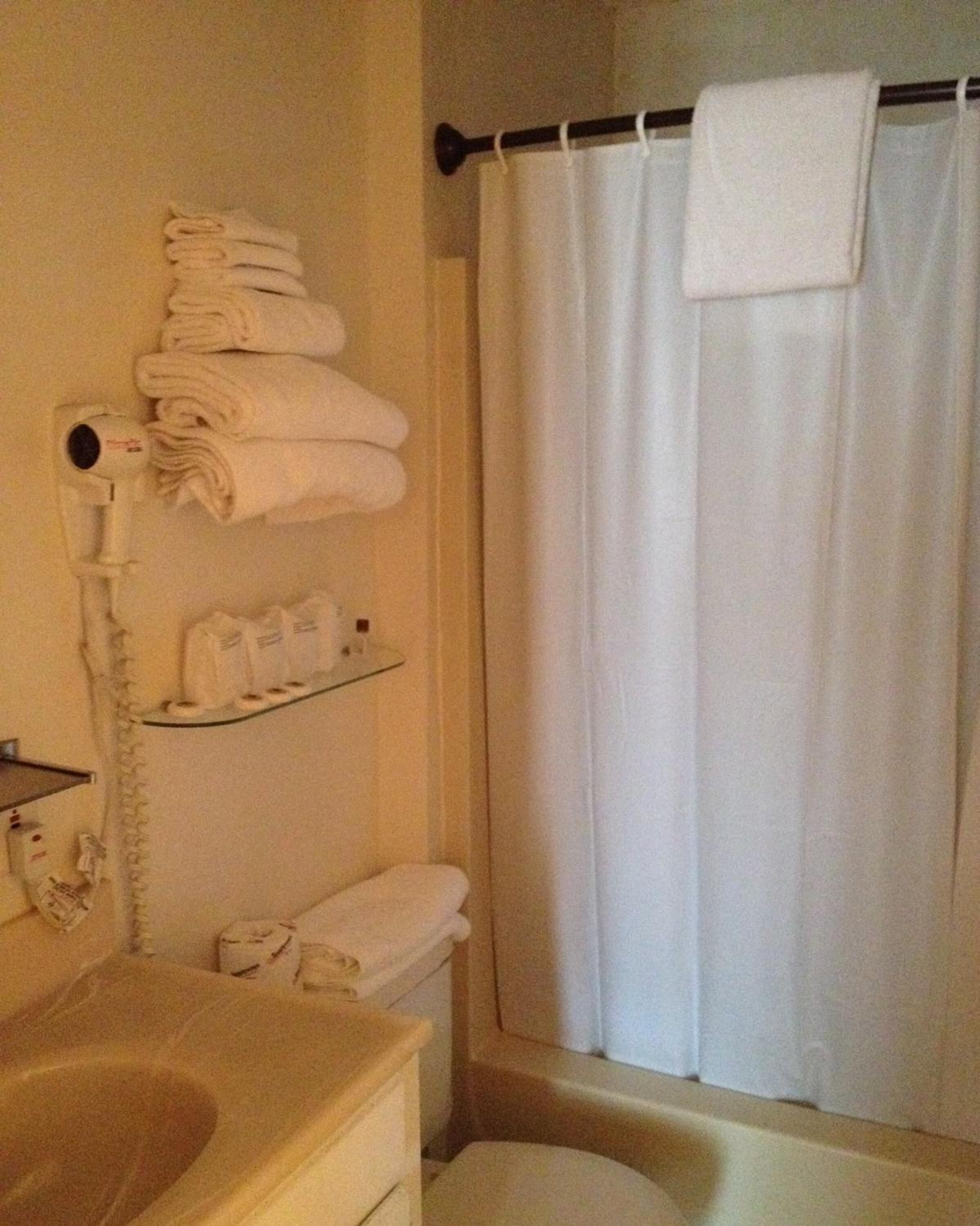 Un bagno con lavandino, wc e tenda per la doccia. Asciugamani impilati su uno scaffale e un asciugacapelli montato a parete.
