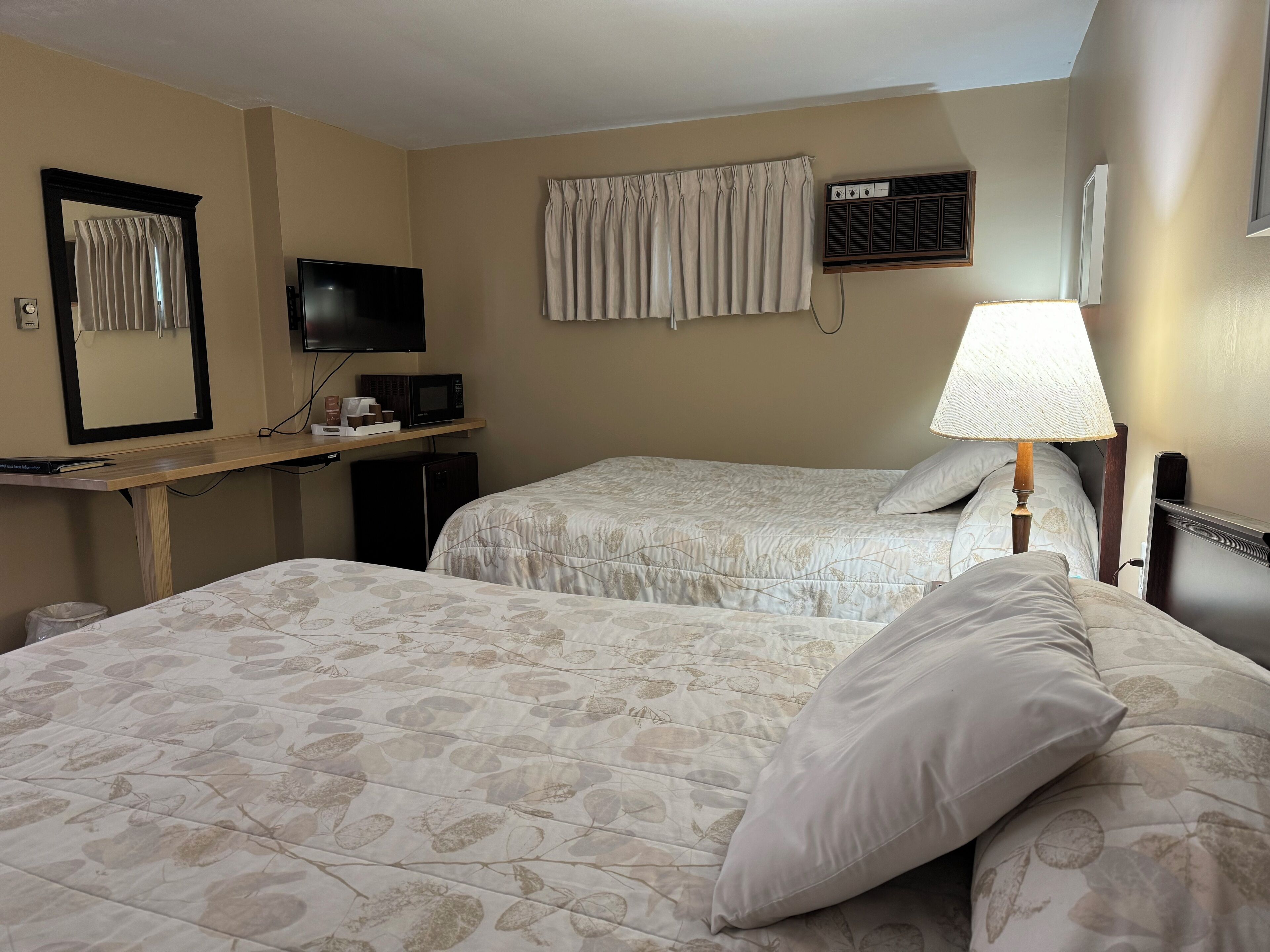Een hotelkamer met twee bedden, een televisie, een magnetron, een bureau en een lamp.
