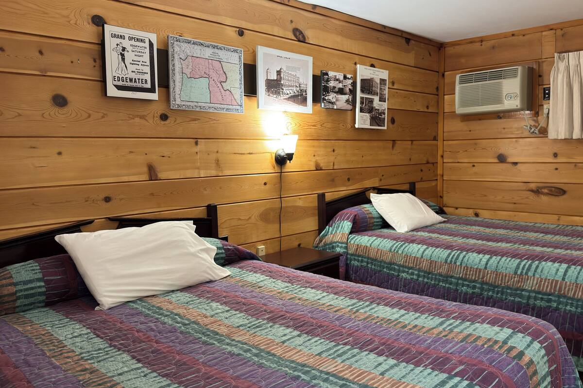 Une chambre avec deux lits, des murs en bois et un climatiseur fixé au mur.