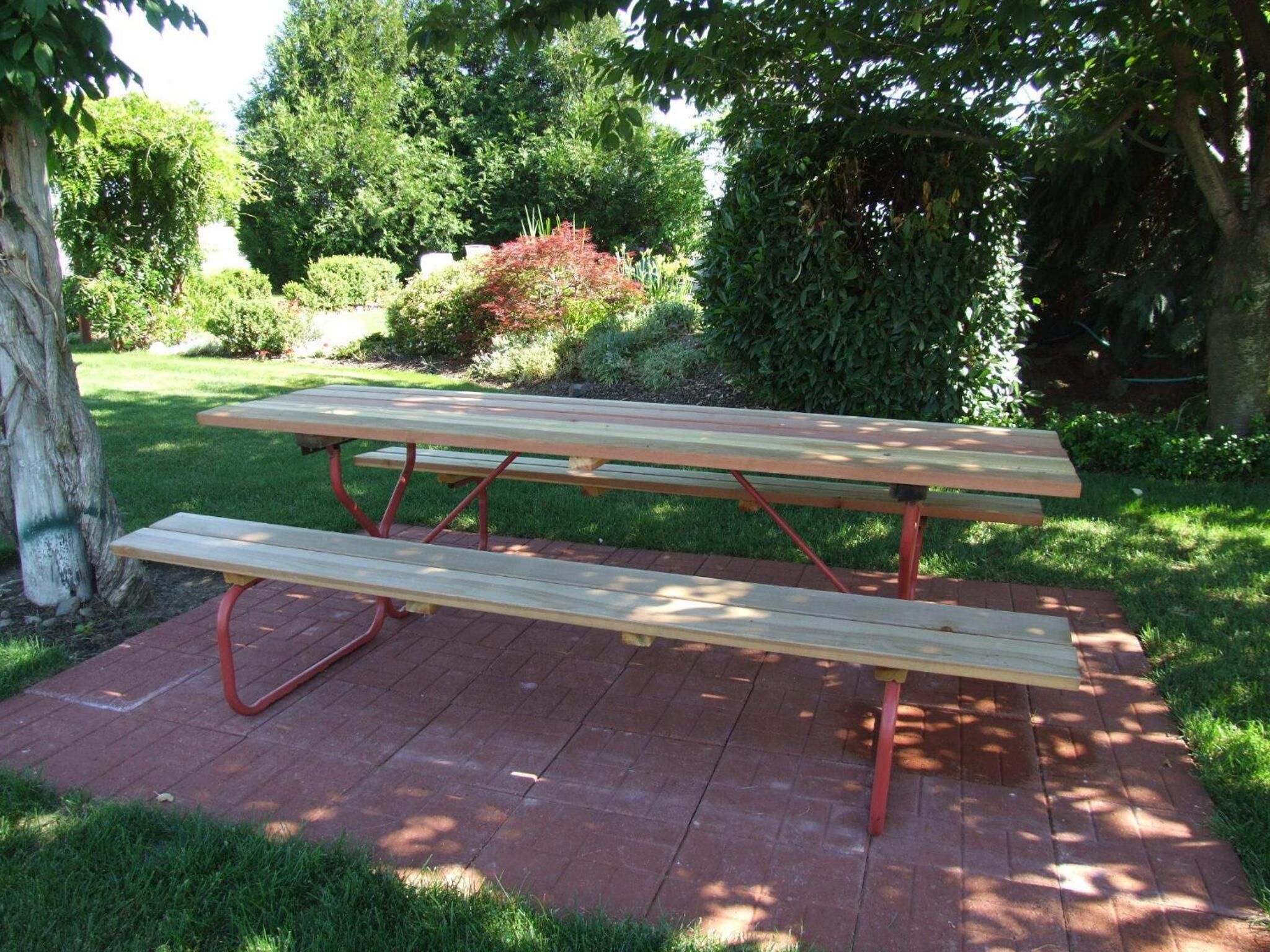 A picnic table with a bench, set on a brick patio surrounded by greenery.