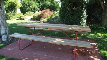 A picnic table with a bench, set on a brick patio surrounded by greenery.