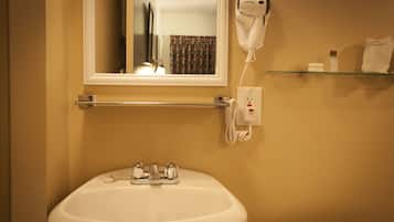 A bathroom with a white sink, a hairdryer mounted on the wall, and a glass shelf with toiletries.
