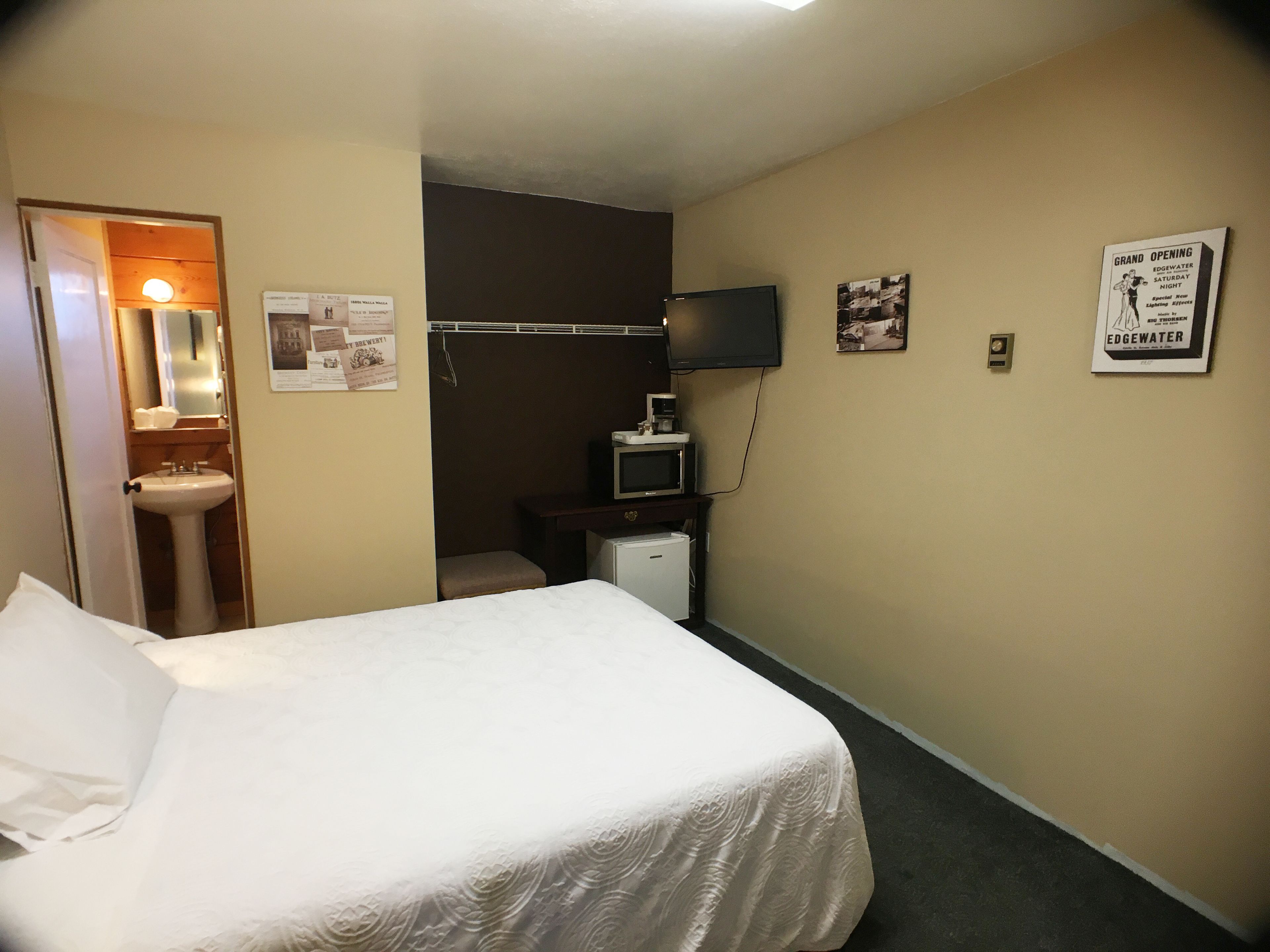 A hotel room with a bed, a television, a small desk, a mirror, and a sink.
