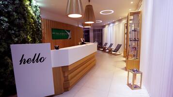A reception area with a wooden reception desk, a green sign, and a seating area with chairs and a small table.