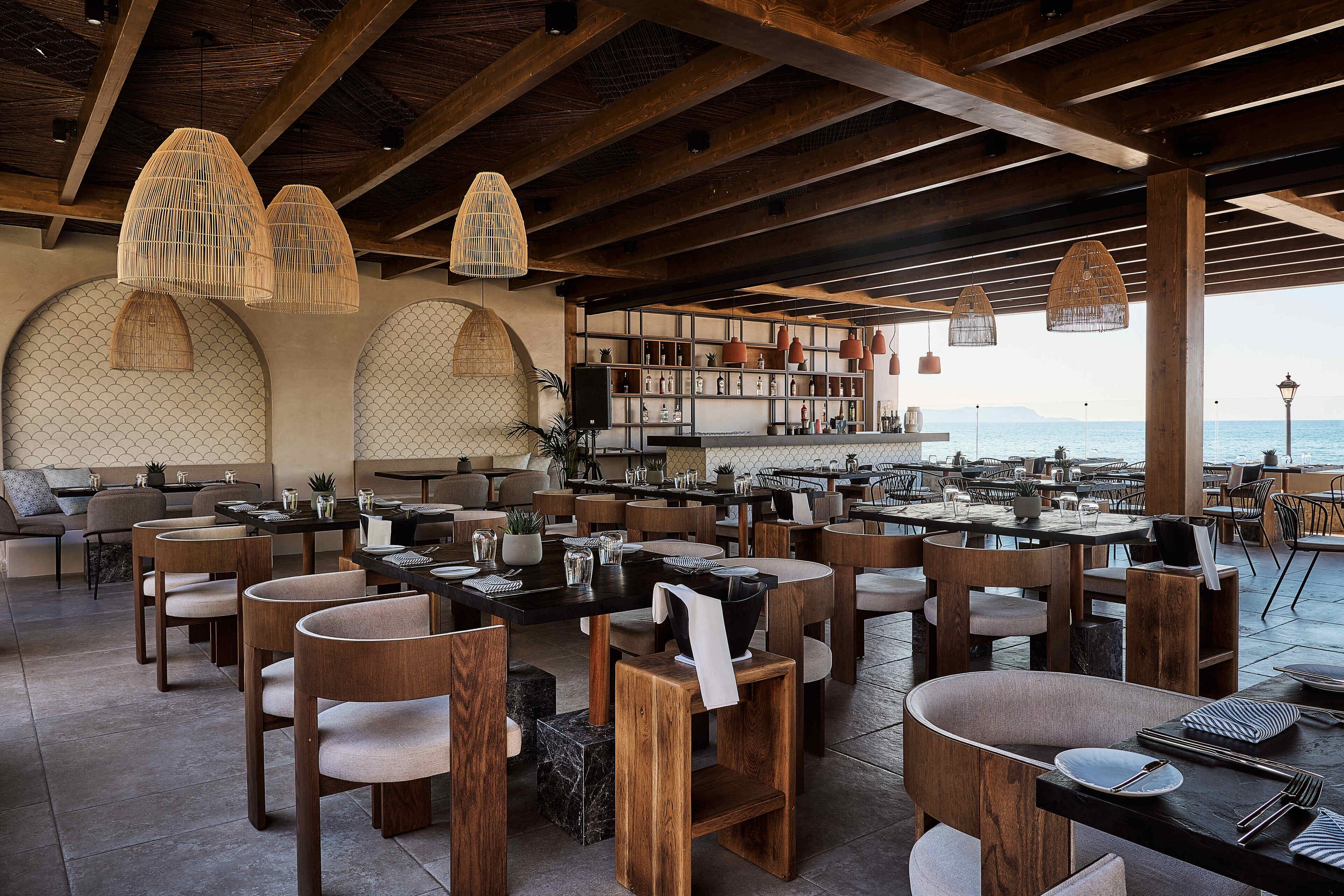 A restaurant with wooden furniture, hanging light fixtures, and a view of the sea.