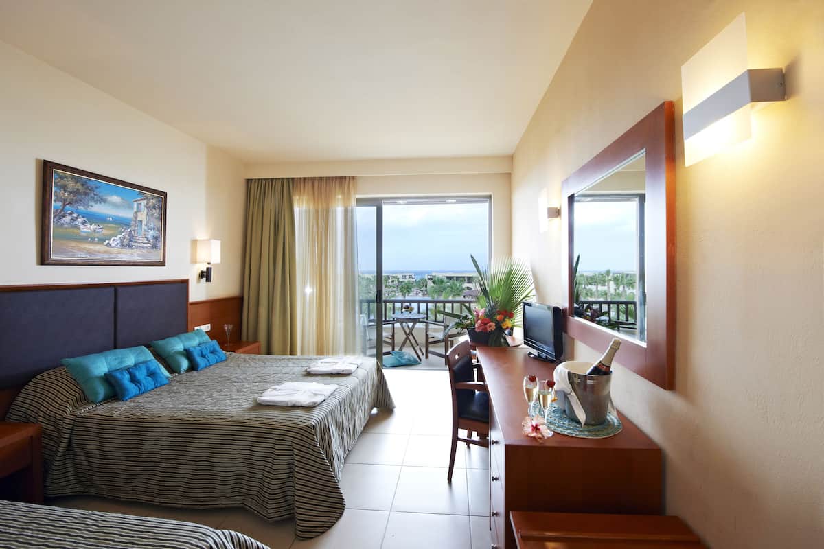 Een hotelkamer met een bed, een bureau met een televisie, een balkon met uitzicht en een schilderij aan de muur.
