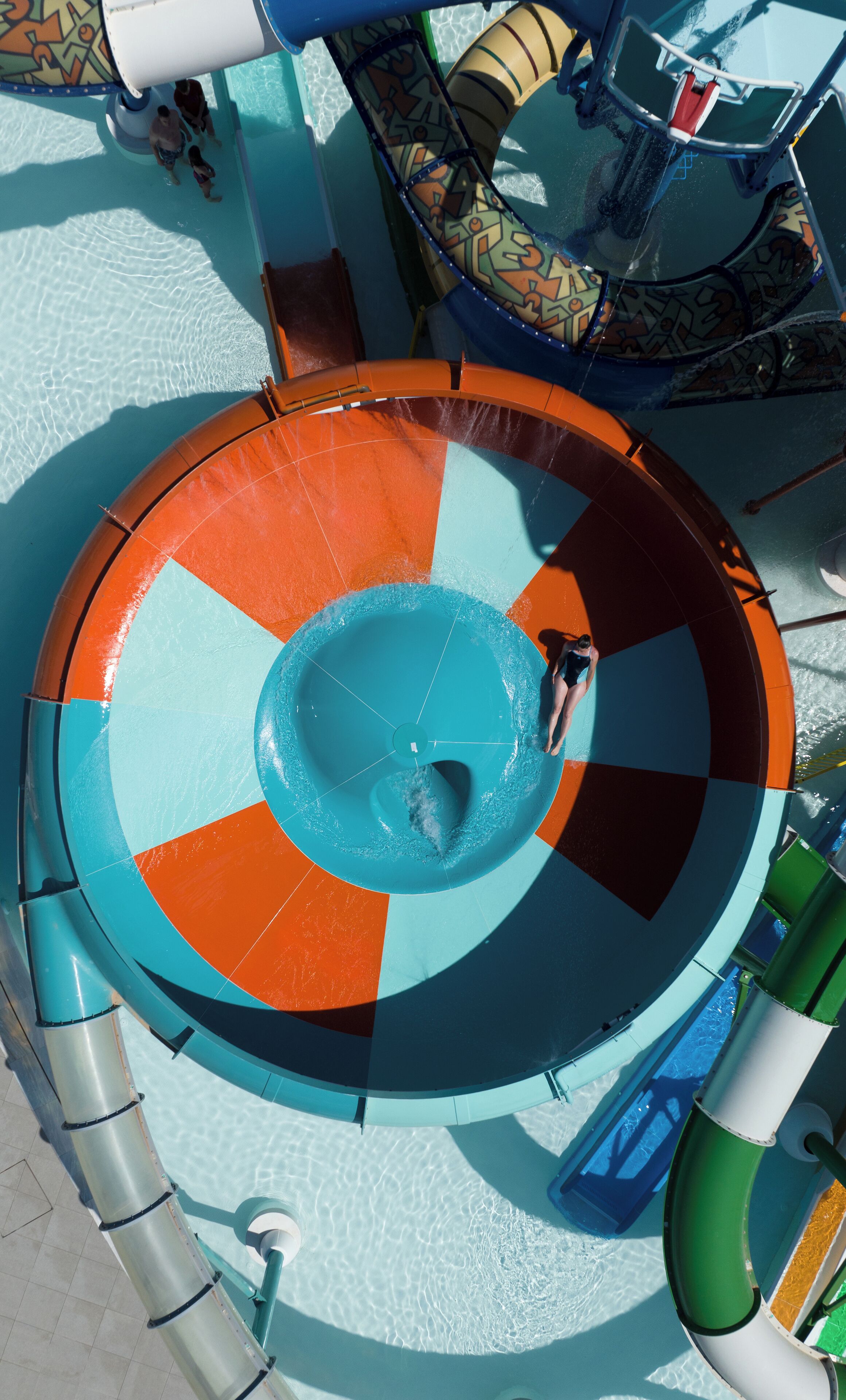A circular water slide with a central blue area and surrounding orange and teal segments.