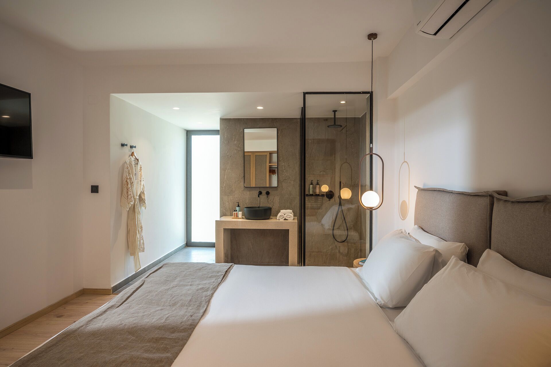 A modern hotel room with a large bed, a bathroom with a mirror and sink, and a TV mounted on the wall.
