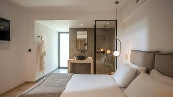 A modern hotel room with a large bed, a bathroom with a mirror and sink, and a TV mounted on the wall.