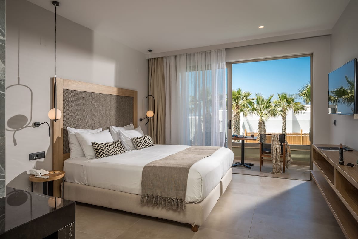 Een moderne hotelkamer met een groot bed, een bureau en een balkon met uitzicht op palmbomen.