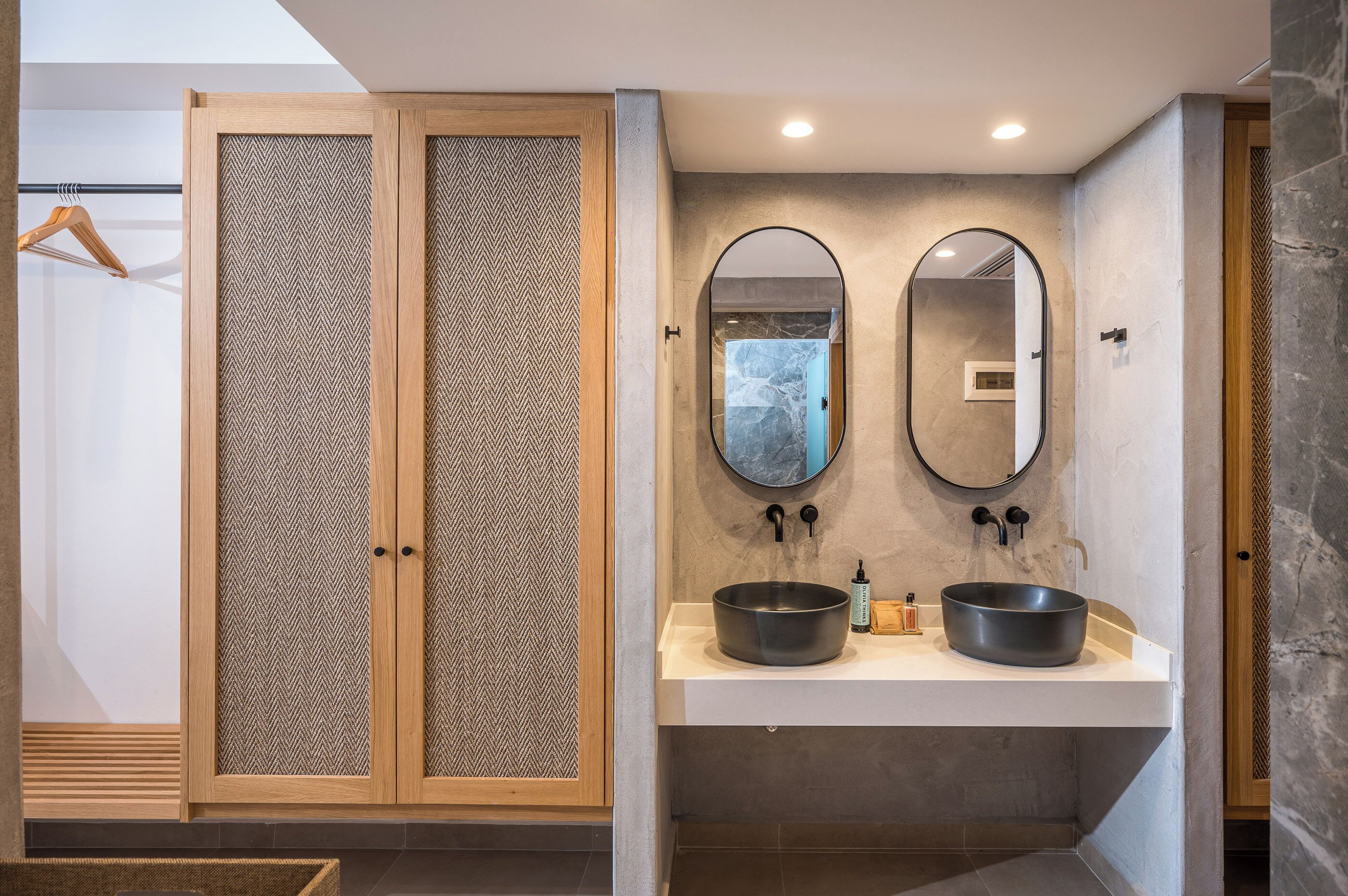 A modern bathroom with a wooden wardrobe, two round mirrors, and a central sink.