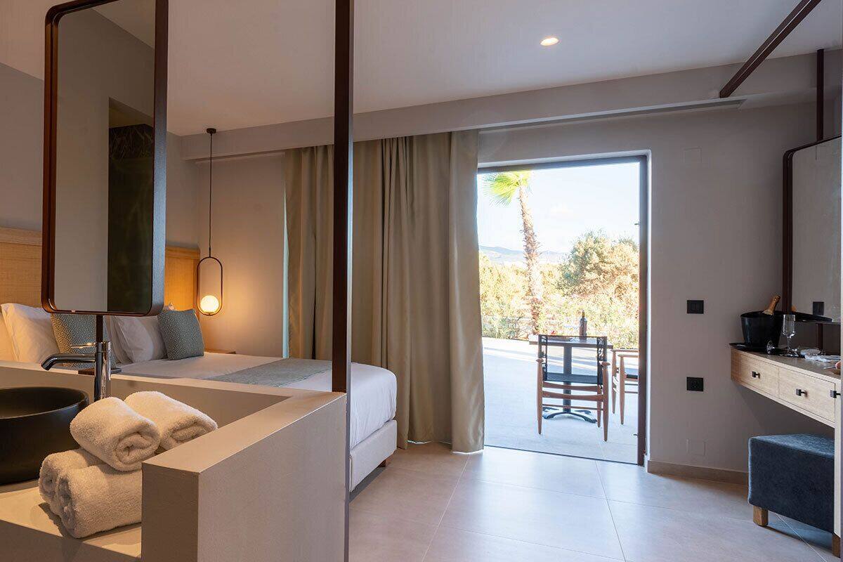 Een moderne hotelkamer met een groot bed, een badkamer met wastafel en spiegel, en uitzicht op de omgeving.