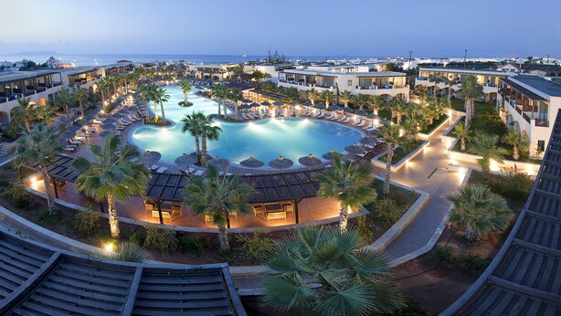A resort with a central swimming pool, multiple guest rooms, and palm trees. - Stella Palace Aqua Park Resort (Hersonissos)