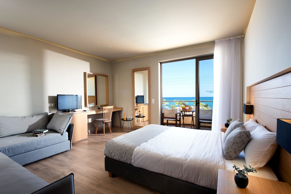 Een moderne hotelkamer met een bed, een bank, een bureau en uitzicht op zee.