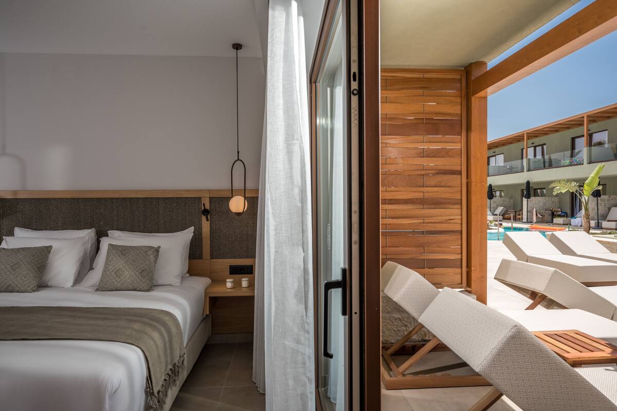 Een moderne hotelkamer met een groot bed, een nachtkastje en uitzicht op een zwembad.
