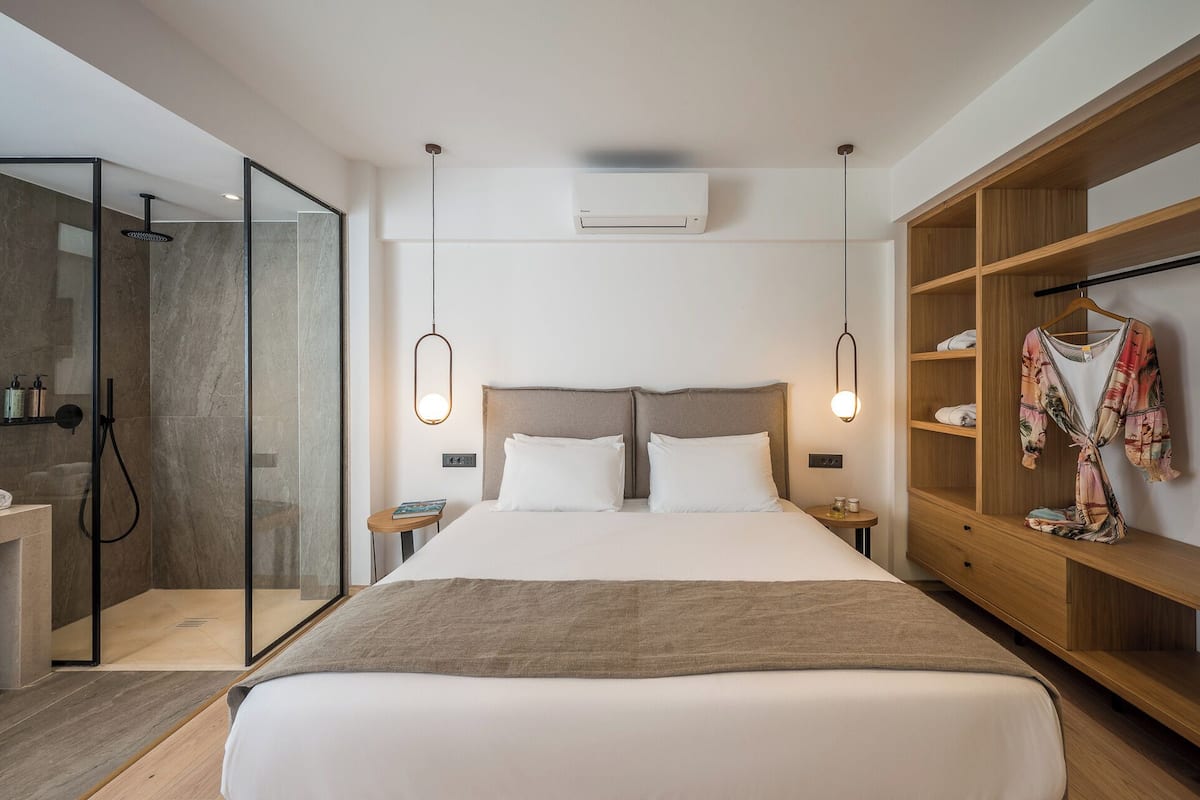 Een moderne hotelkamer met een groot bed, een inloopdouche, een houten garderobe en een wandairconditioner.