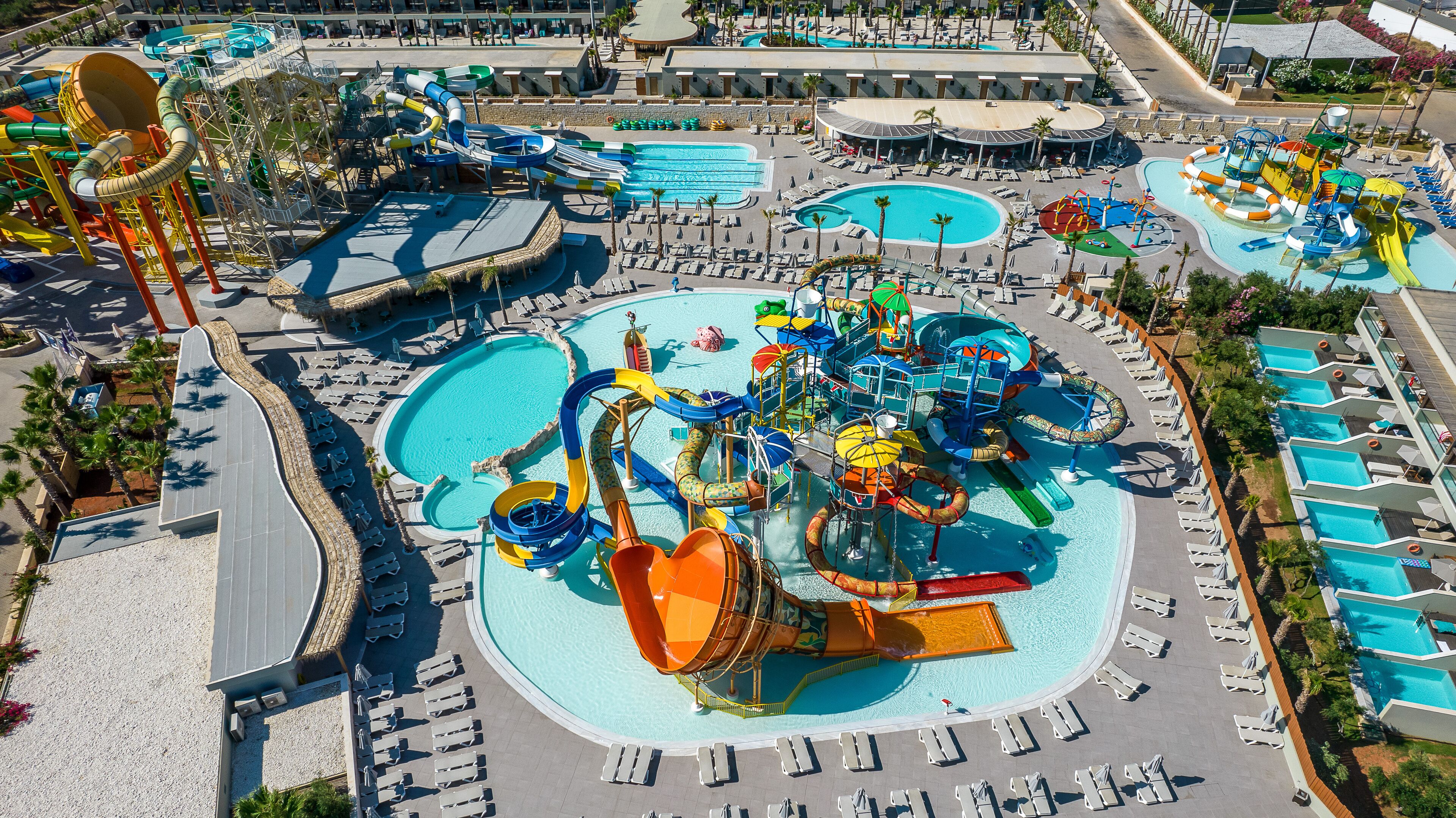 Een waterpark met glijbanen en zwembaden, omringd door ligbedden en parasols.