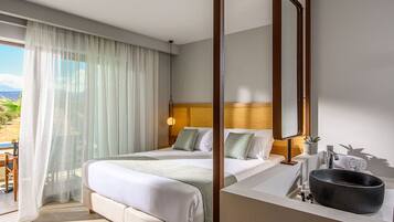 A hotel room with a bed, a bathroom with a sink and a large basin, and a balcony with a view of the countryside.
