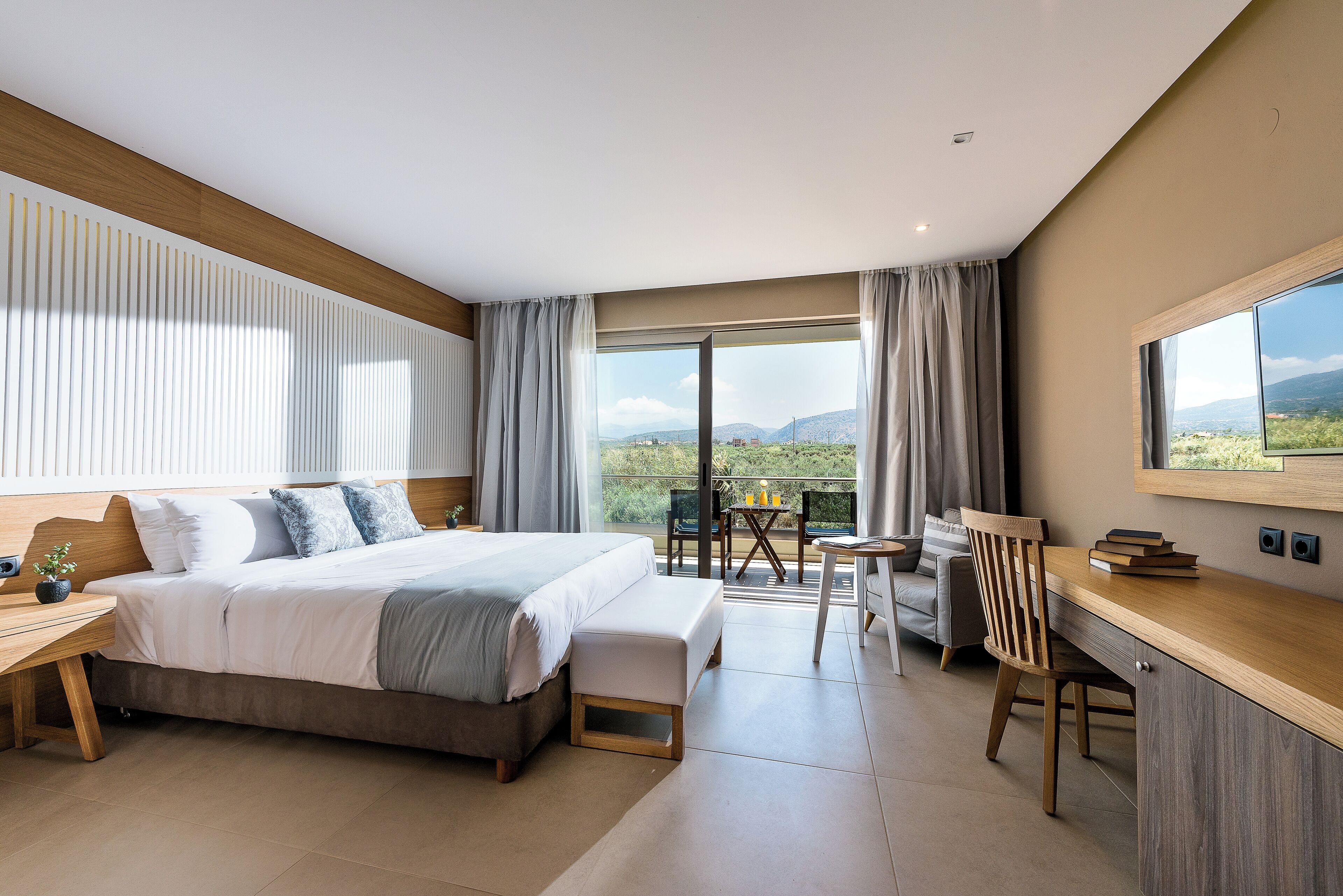A modern hotel room with a large bed, a desk, and a balcony with a view.
