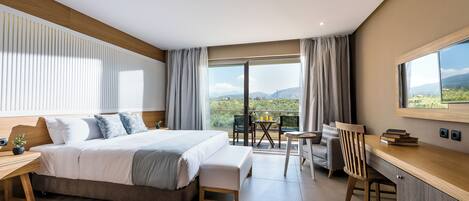A modern hotel room with a large bed, a desk, and a balcony with a view.
