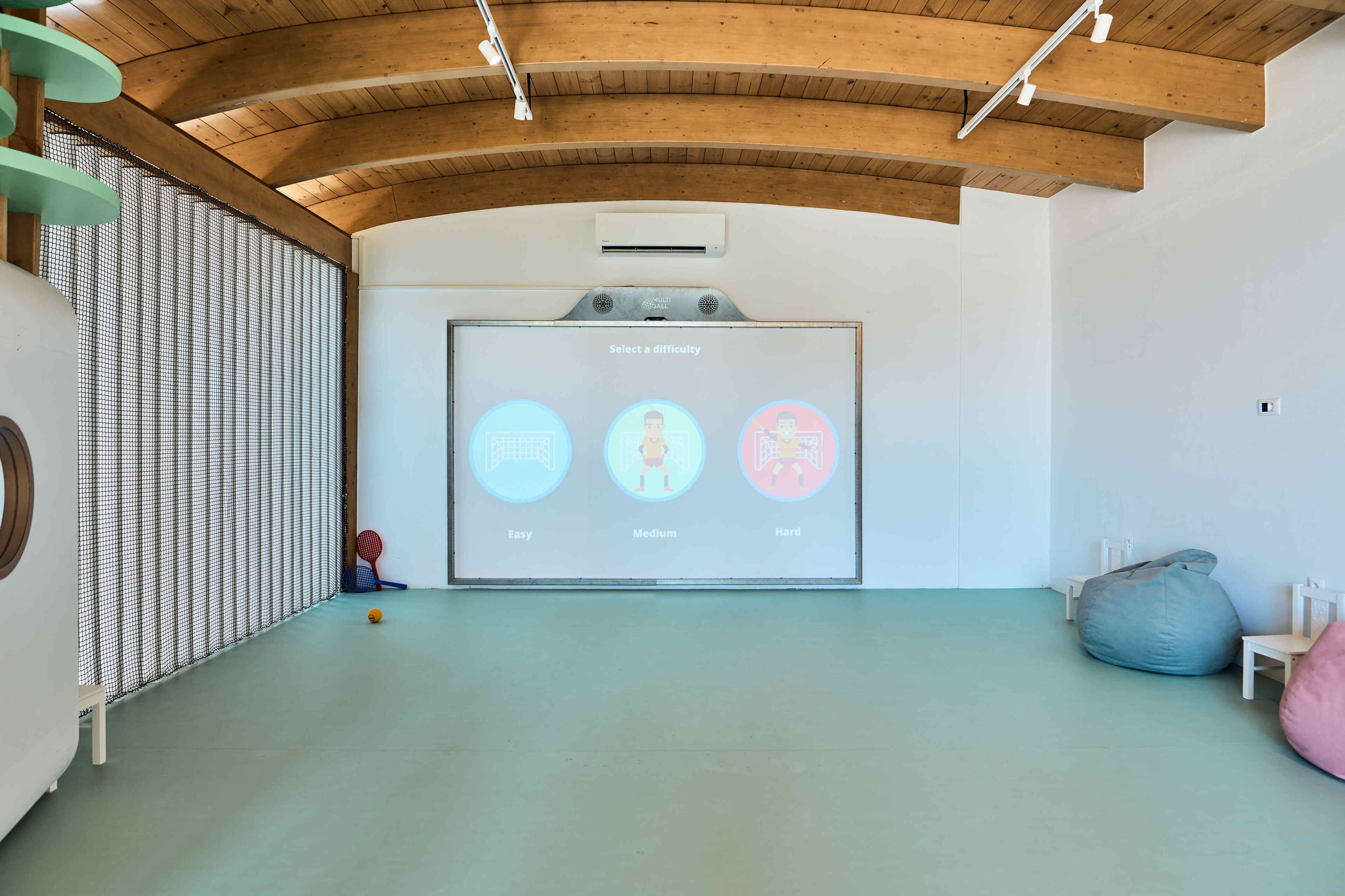 Une pièce spacieuse avec un plafond en bois, un écran de projection affichant les niveaux de difficulté et une table de ping-pong.