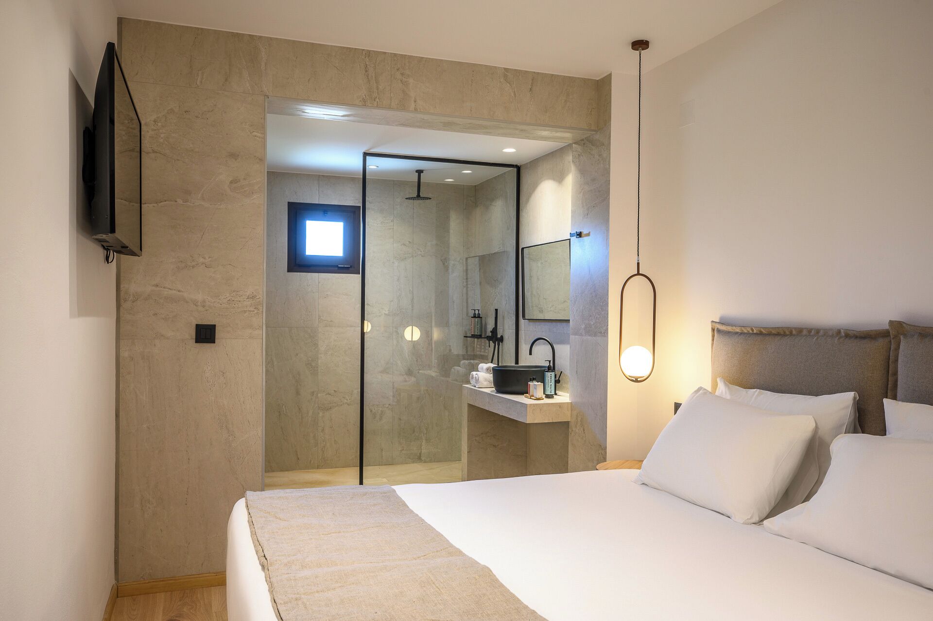 A modern bedroom with a large bed, a bedside table, a mirror, and a TV mounted on the wall.