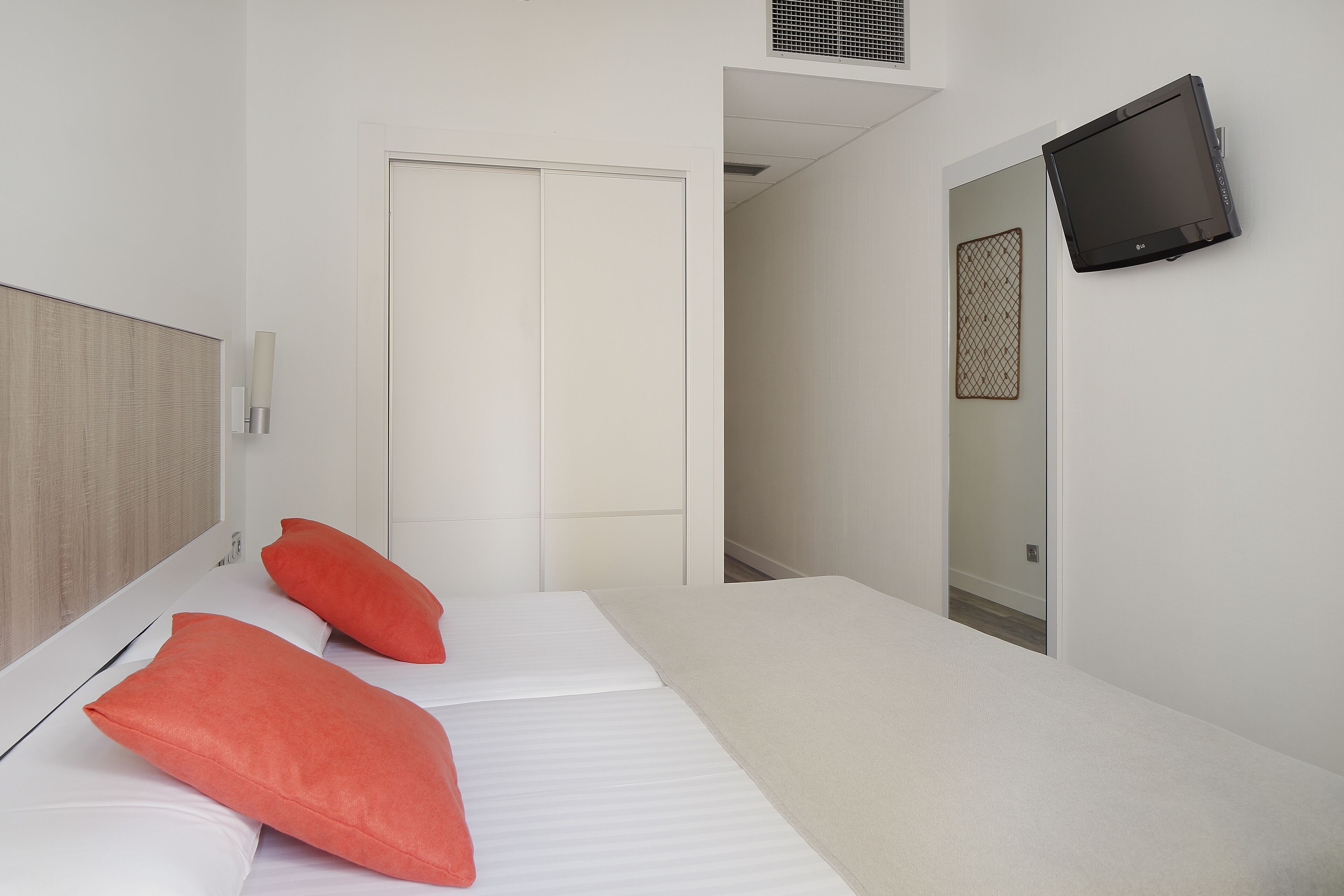 A hotel room with a bed, a television mounted on the wall, and a door leading to another room.