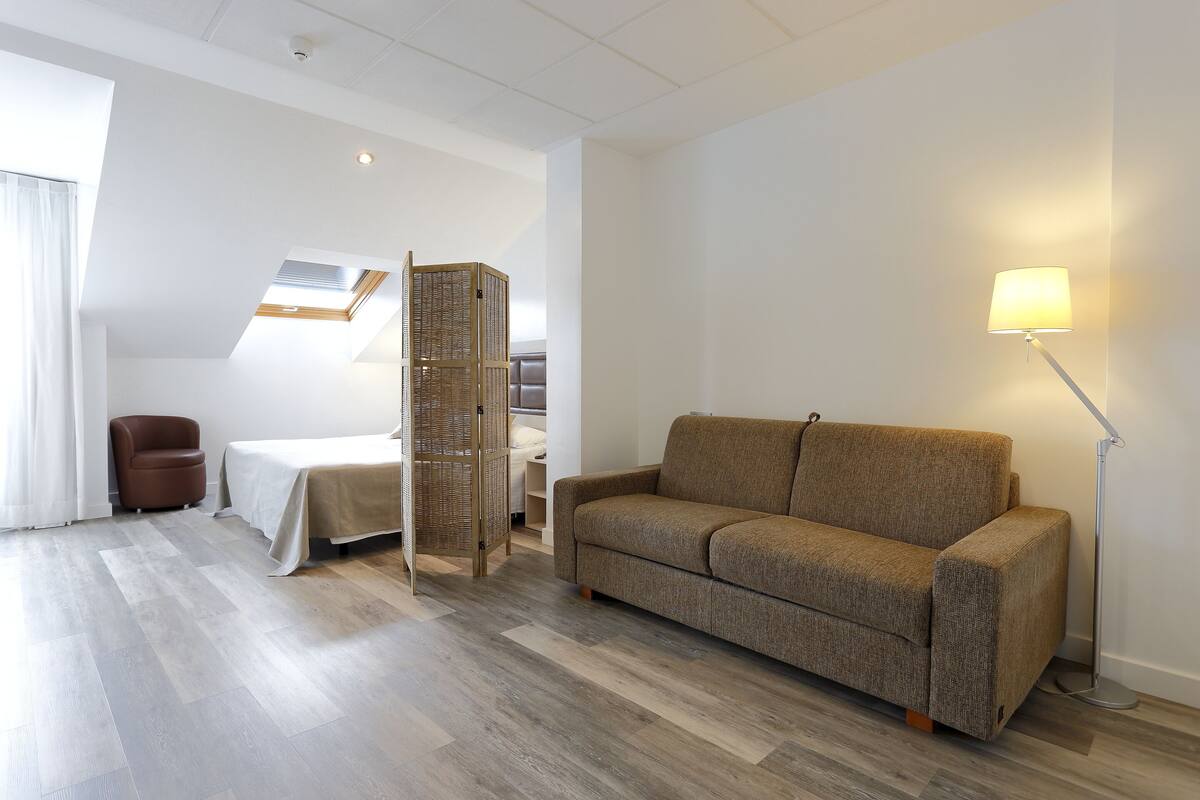 A modern living room with a sofa, a lamp, a chair, and a bed.
