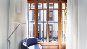 A room with a blue chair, a floor lamp, and a view of a building with blue and white stripes through a glass door. - Hotel Santa Rosa, Blue Hoteles (Gijon)