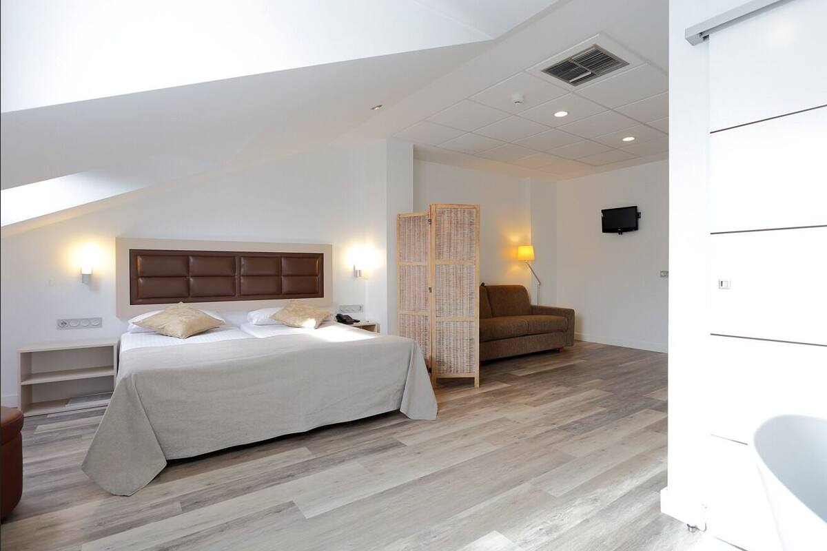 A bedroom with a bed, a chair, a bedside table, a lamp, and a television.