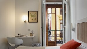 A hotel room with a bed, a desk with a chair, a small stool, a framed botanical print on the wall, and a balcony with a view of buildings. - Hotel Santa Rosa, Blue Hoteles (Gijon)