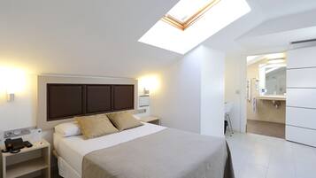 A modern hotel room with a bed, bedside table with a phone, a nightstand, a skylight, and a bathroom with a sink and mirror.
