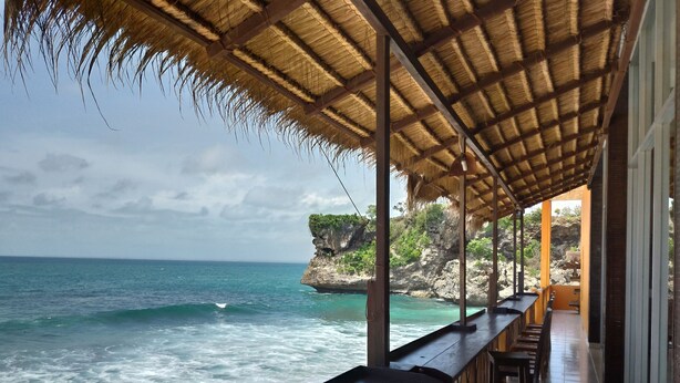 A beachside restaurant with a thatched roof, overlooking the ocean and a rocky cliff. - Balangan Paradise Hostel and Restaurant (Jimbaran)