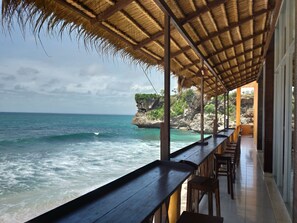 A beachside restaurant with a thatched roof, overlooking the ocean and a rocky cliff. - Balangan Paradise Hostel and Restaurant (Jimbaran)