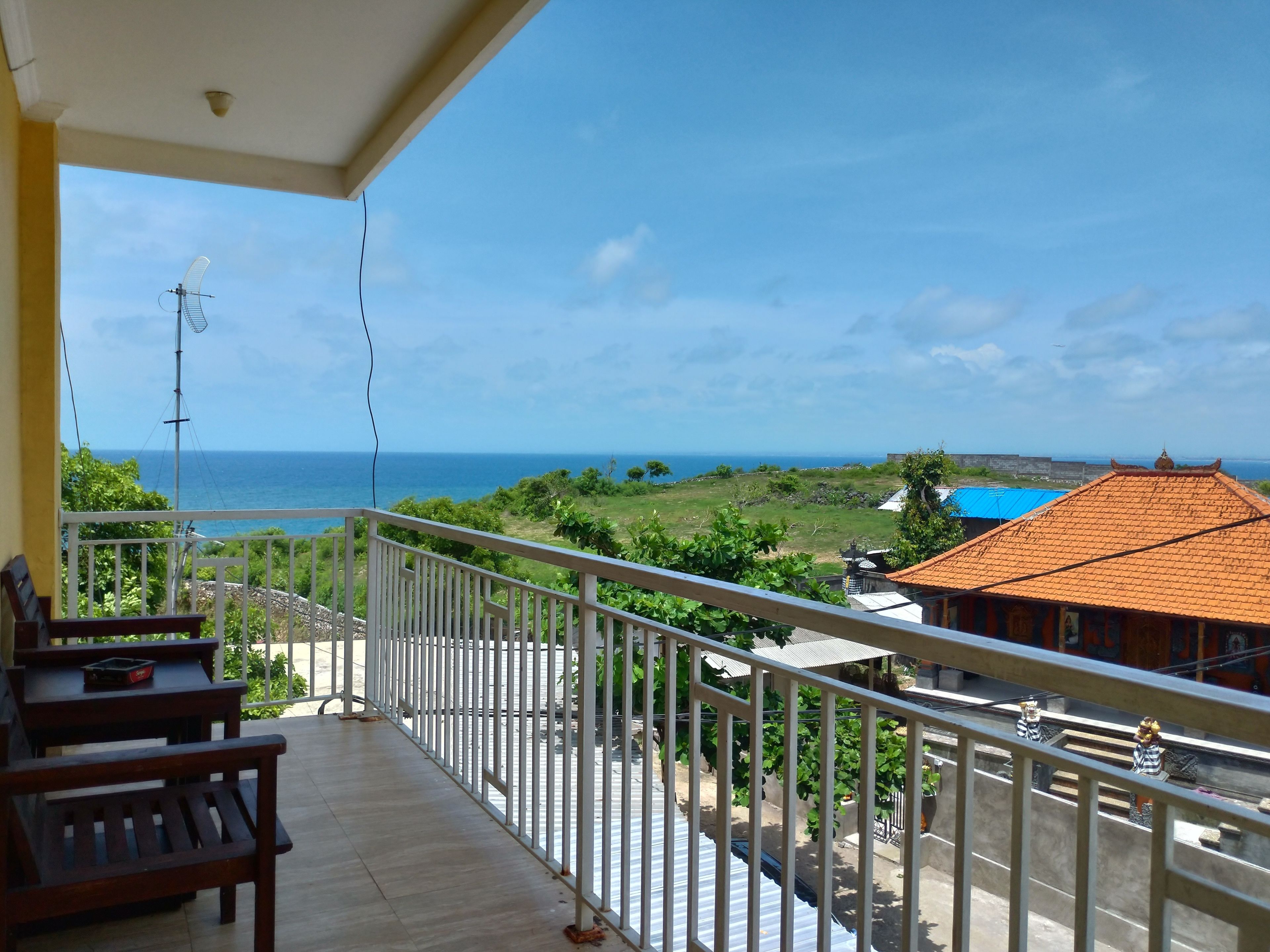 A balcony with a view of the sea, a tiled roof, and a small garden area.