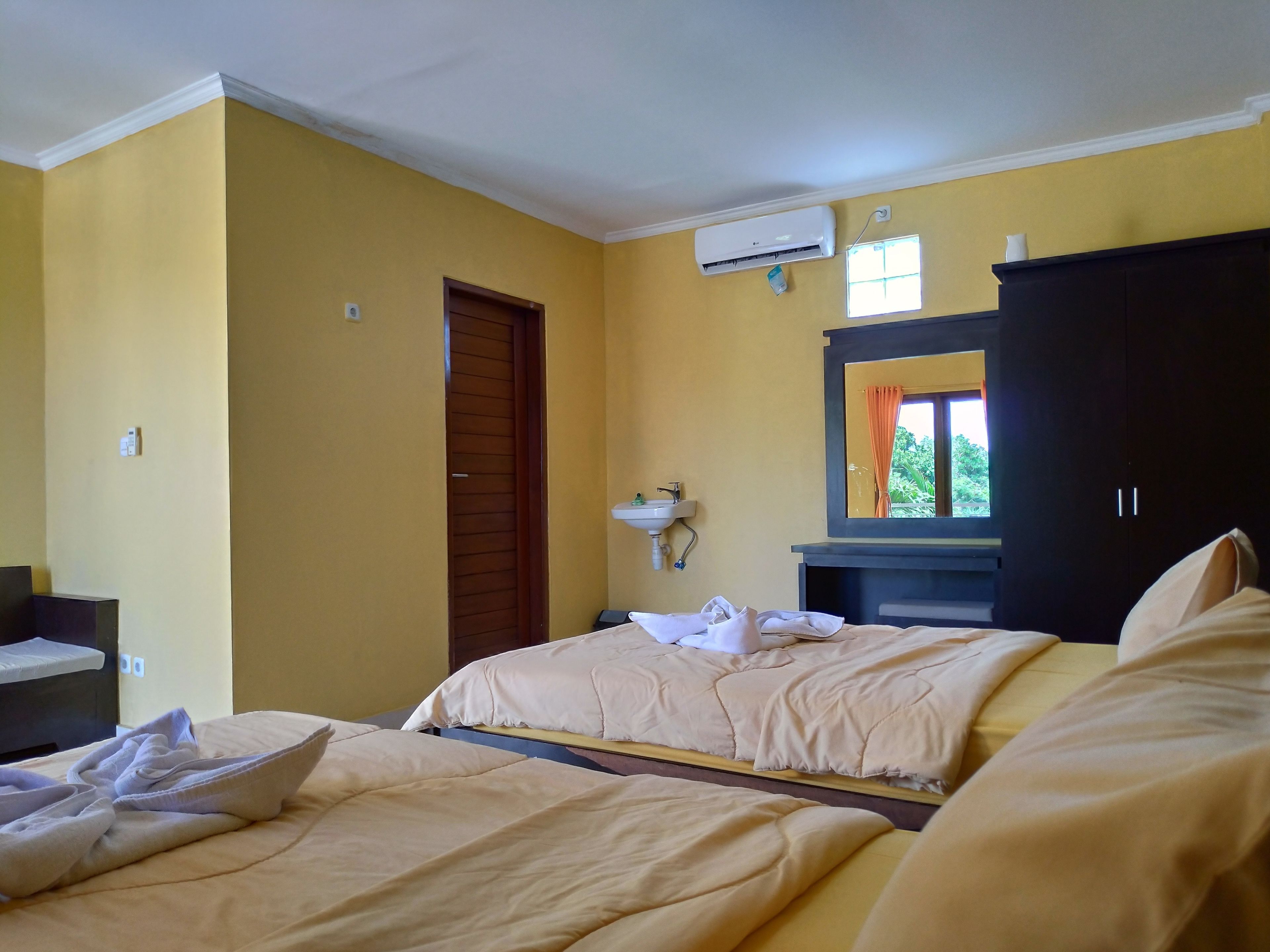 A hotel room with two beds, a bathroom with a sink and mirror, and an air conditioning unit on the wall.