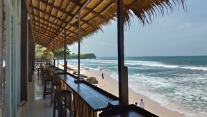 A beachside restaurant with a thatched roof, outdoor seating, and a view of the ocean. - Balangan Paradise Hostel and Restaurant (Jimbaran)