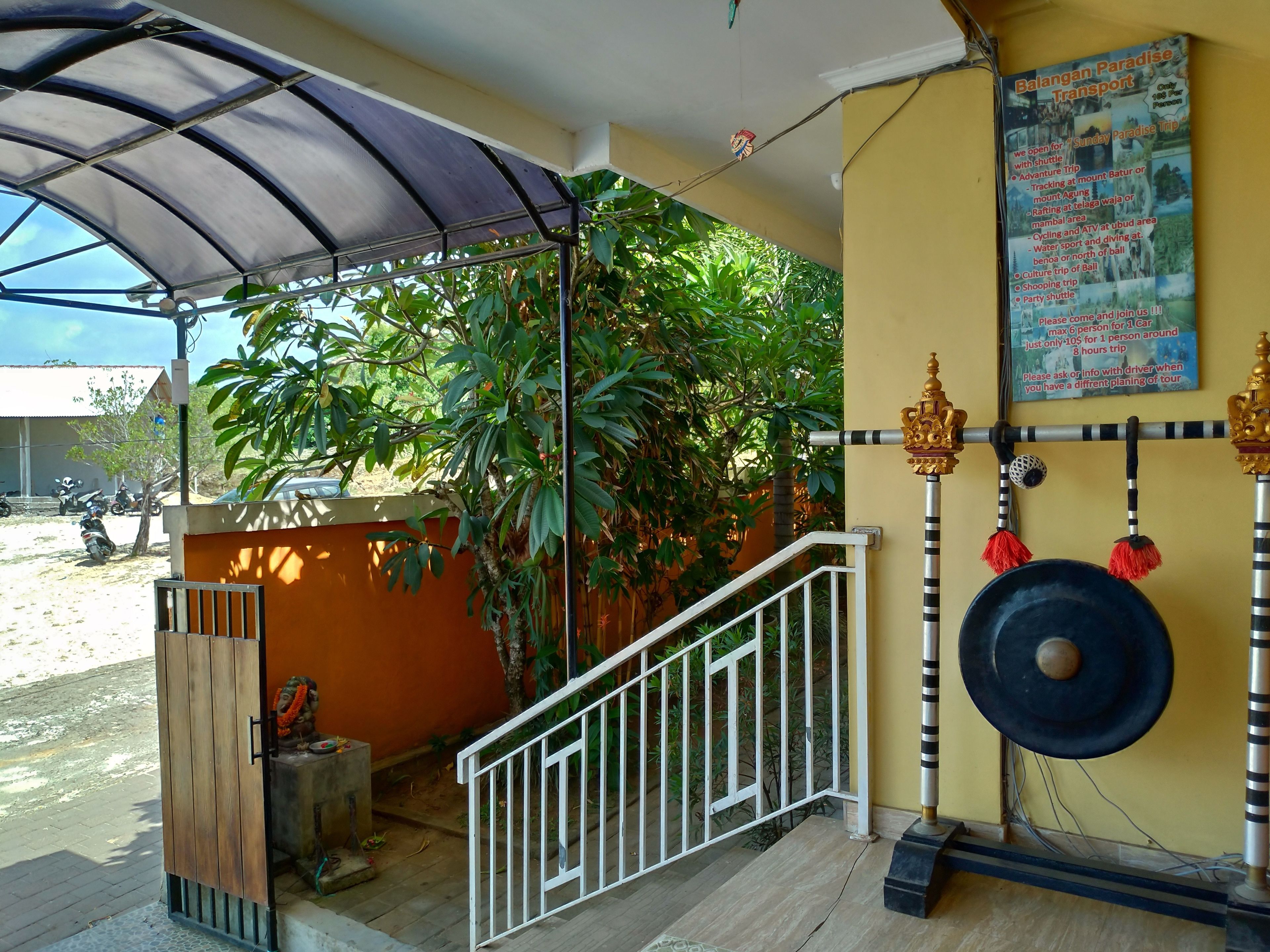 A covered outdoor area with a staircase, a wall-mounted decoration, and a poster advertising a transport service.