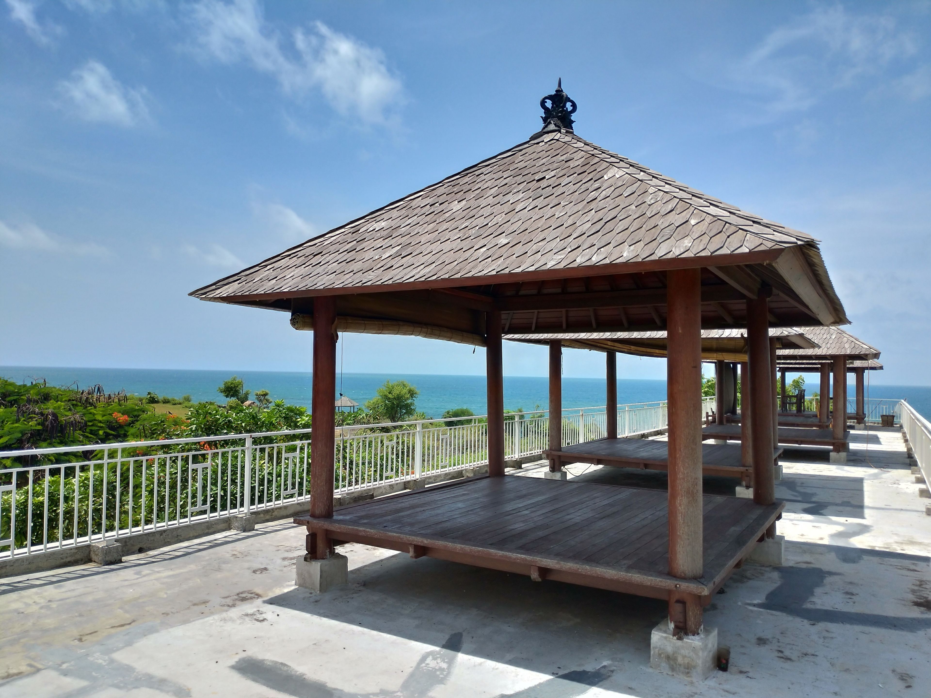 A wooden gazebo with a tiled roof overlooking a coastal area.