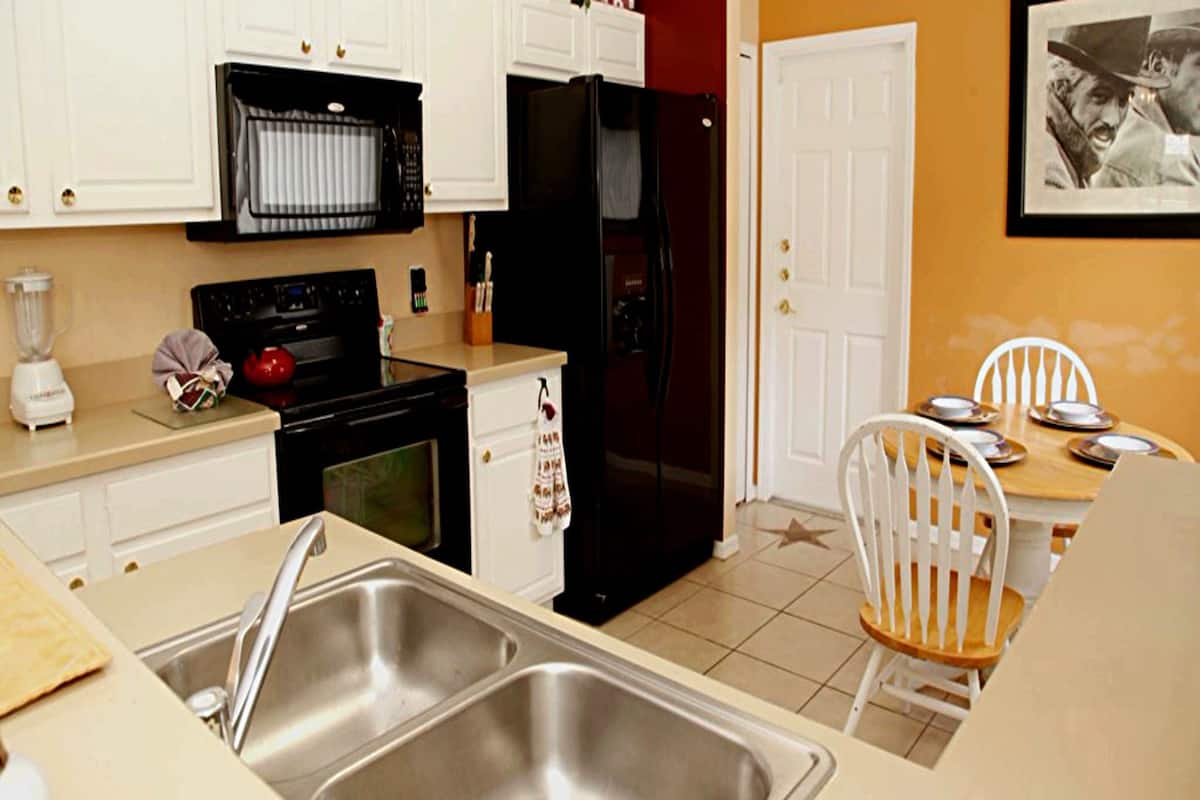 A kitchen with a double sink, stove, refrigerator, and a dining area with a table and chairs.