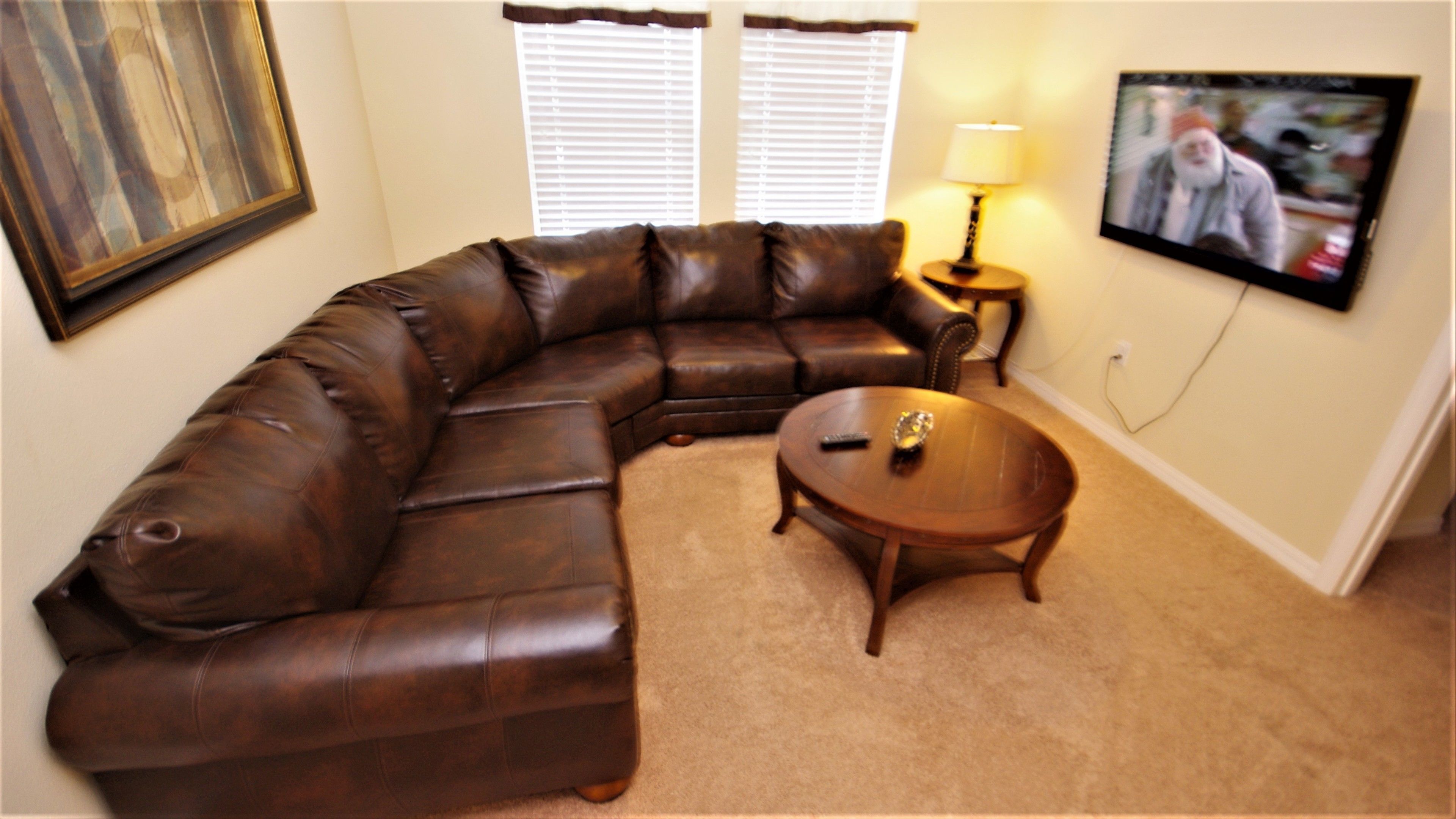 A living room with a brown leather sectional sofa, a wooden coffee table, and a television mounted on the wall.