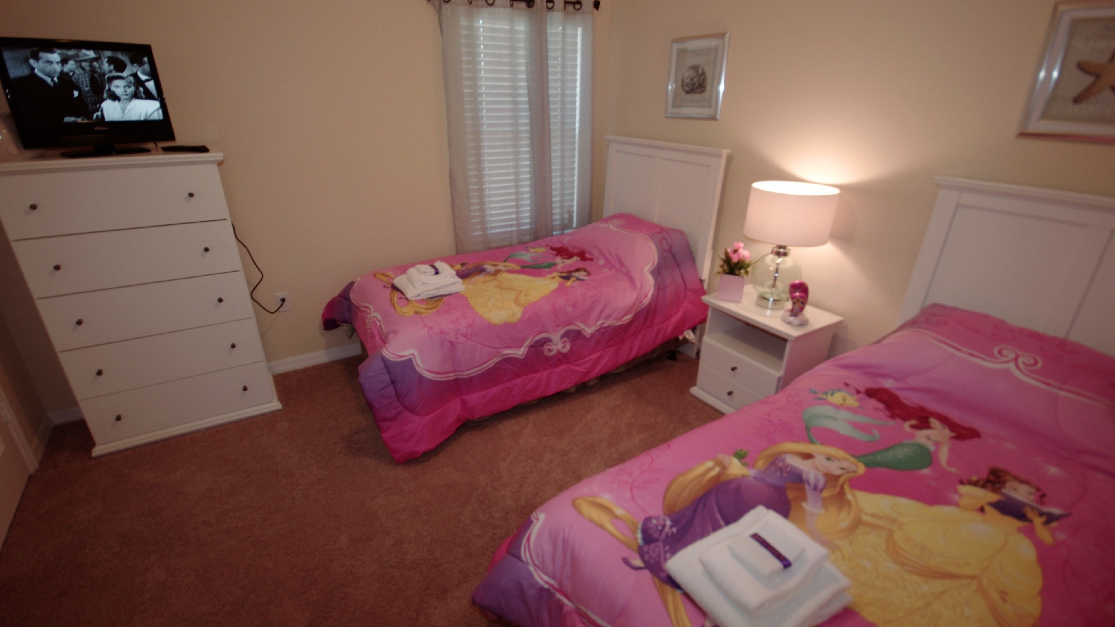 Une chambre avec deux lits, une commode, un téléviseur et une table de chevet avec une lampe.