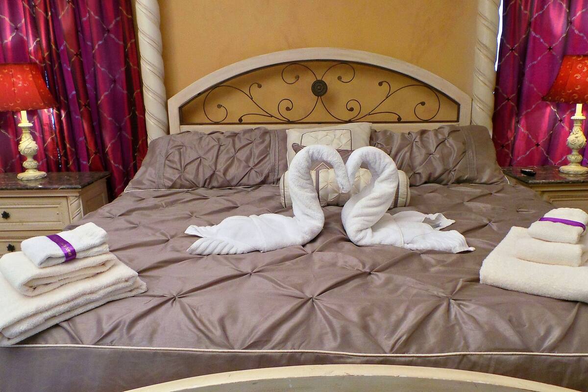 A bed with a headboard, pillows, and two swan-shaped towels.
