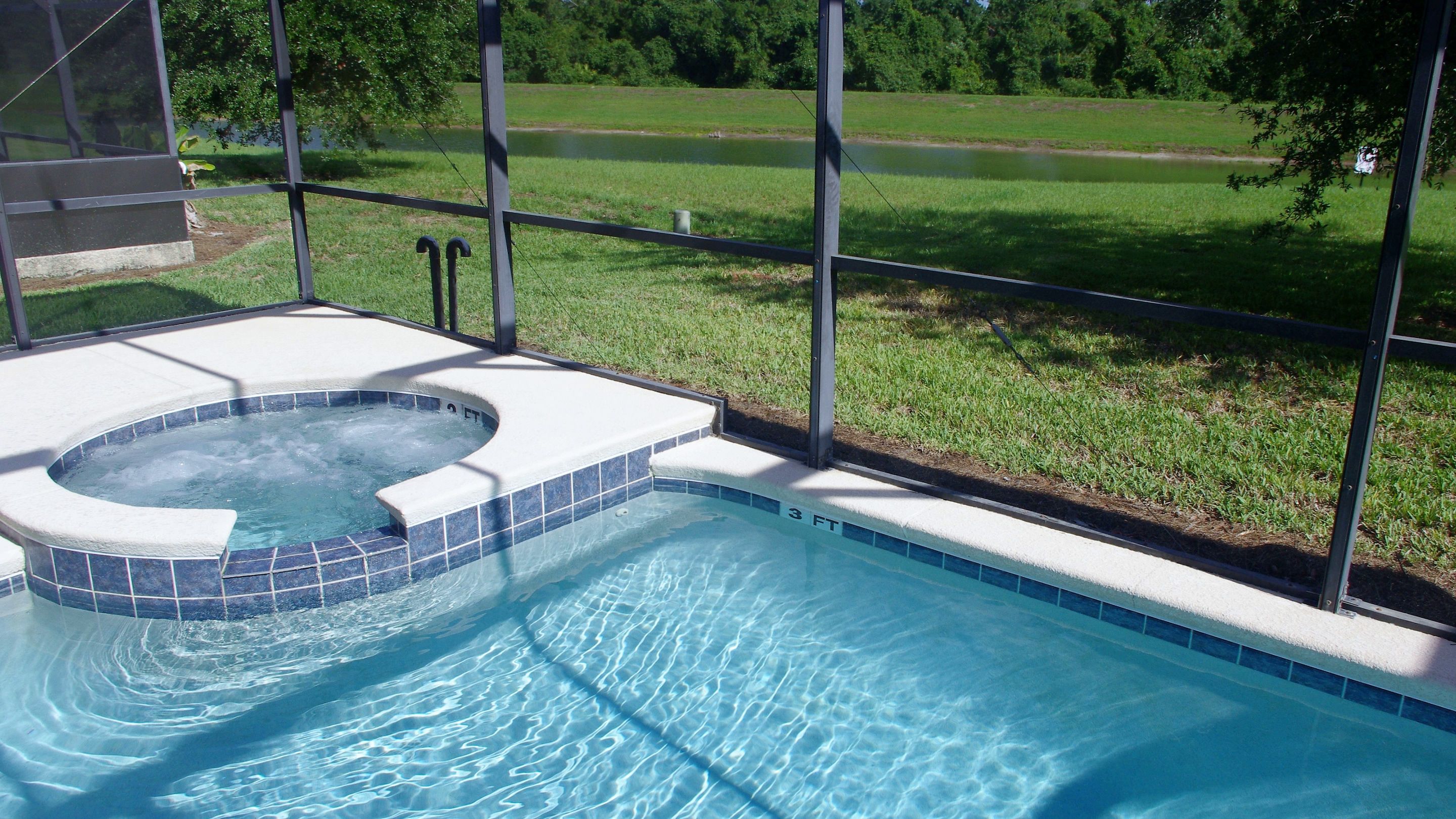 Une piscine avec un espace équipé d’un jacuzzi, le tout entouré d’une clôture et d’un terrain herbeux.