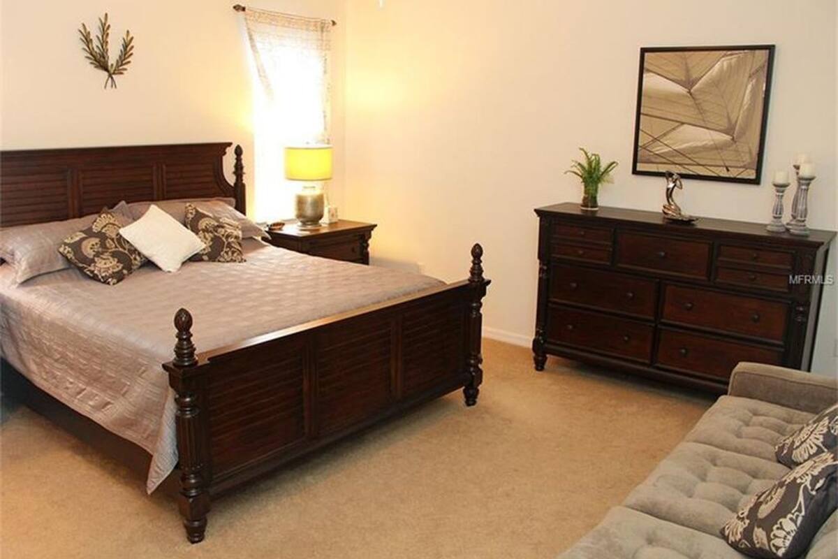 A bedroom with a wooden bed, a dresser, a lamp, and a framed picture on the wall.