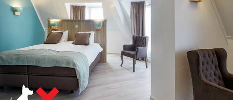 A modern hotel room with a large bed, two chairs, and a view of the city.