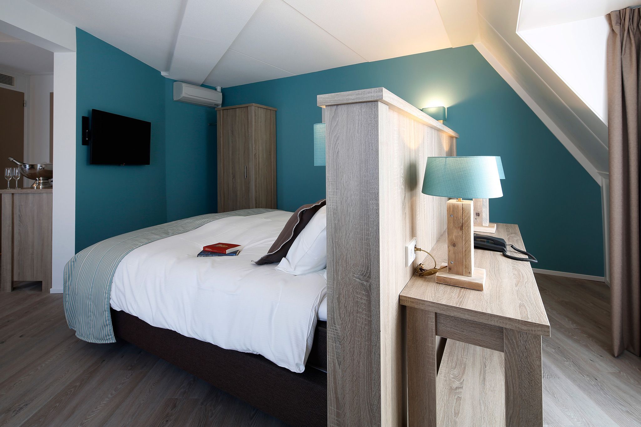 Une chambre à coucher moderne avec un lit, un bureau doté d’une lampe, une télévision et une armoire.