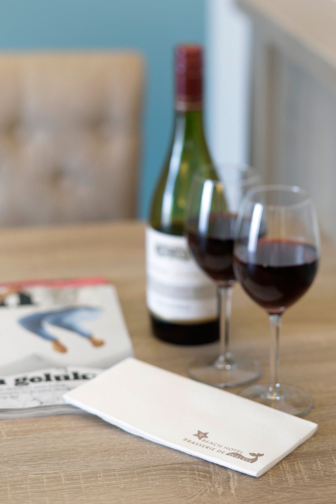 Una botella de vino, dos copas de vino y un menú sobre una mesa de madera.
