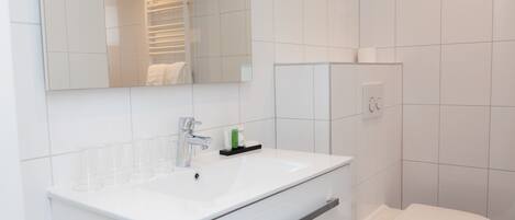 A modern bathroom with a white sink, mirror, and toilet.