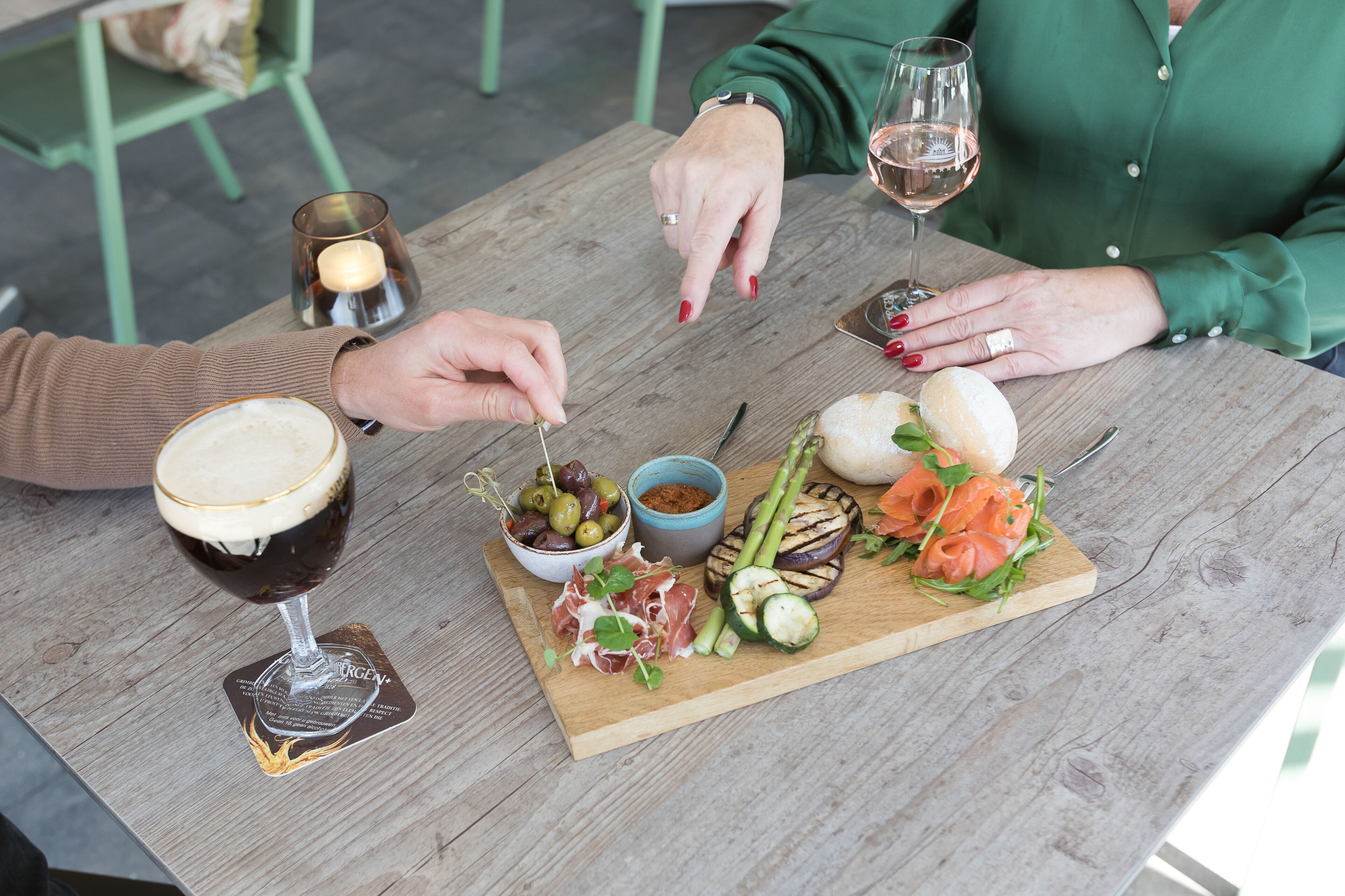 A wooden table with a glass of wine, a plate of food including grilled vegetables and meat, and a candle.